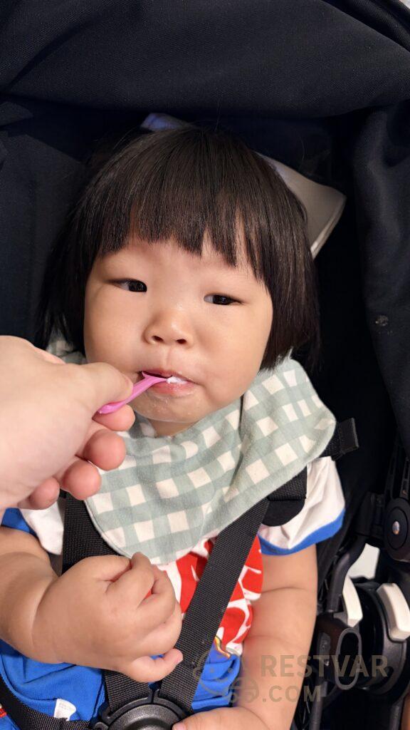 유모차에 앉은 아기에게 분홍 스푼으로 아이스크림을 떠먹이는 모습