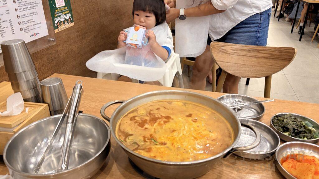 칼제비 냄비가 놓인 식탁과 아기 의자에 앉아 일회용 턱받이를 한 아이